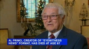 An older man in a suit and tie sits indoors with Christmas trees behind him. Overlay reads: Al Primo, creator of Eyewitness News, dies at 87.