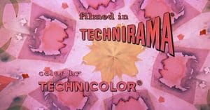 Kaleidoscopic pink and yellow background with text: filmed in TECHNIRAMA® and color by TECHNICOLOR® in bold, vintage-style fonts.
