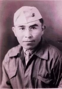 Black-and-white portrait of a man wearing glasses, a military uniform, and a cap, looking directly at the camera with a neutral expression.