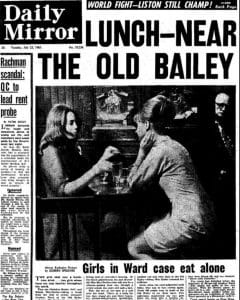 Two women sit at a small restaurant table with drinks, facing each other, as a man stands in the background. The newspaper headline above reads, “LUNCH—NEAR THE OLD BAILEY. Girls in Ward case eat alone.”.
