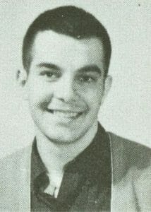 A young man with short dark hair smiles at the camera in a collared shirt and jacket. Black and white, vintage yearbook style.