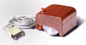 A vintage wooden computer mouse with a red button on top, a metal ball underneath, and a cable with a connector attached, displayed on a white surface.