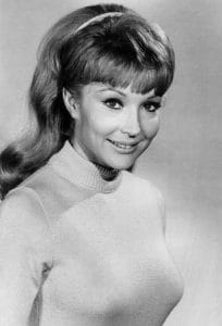 Black and white professional headshot of a woman with long hair, wearing a light-colored turtleneck sweater, smiling gently and looking slightly to the side.