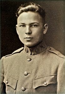 Young man in an early 20th-century military uniform poses for a formal black-and-white portrait, looking directly at the camera with a neutral expression.