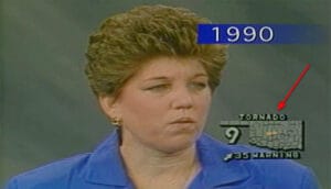 A woman with short brown hair in a blue blazer appears on TV with “1990” and “TORNADO WARNING” weather graphics onscreen.