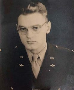 Black and white portrait of a young man in glasses and a U.S. military uniform, facing the camera against a plain background.