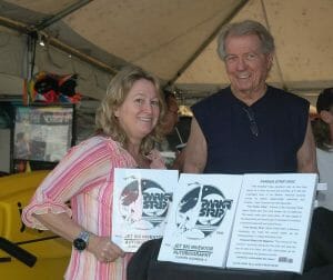 A smiling woman and older man stand indoors by a display with two Jet Ski Inventor Autobiography books showing Parker Strip logos.