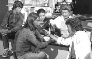Five people in a black-and-white diner scene; a man points at another while a woman and two kids watch, evoking an old TV show.