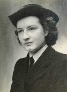 Black and white portrait of a young woman in a uniform jacket, tie, white shirt, and peaked cap, gazing slightly sideways, neutral-faced.