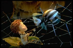 A claymation boy sits on a green leaf, reaching toward a striped spider with a human-like face and blue hat against a web.