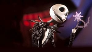 A skeleton in a black pinstripe suit curiously examines a delicate snowflake against a dark, blurred background.