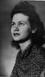 Black and white portrait of a young woman with wavy hair in a patterned blouse, gazing upward thoughtfully against a plain background.