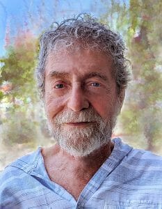 An older man with curly gray hair and a beard smiles gently in a light blue striped shirt, outdoors with trees and sky blurred behind him.