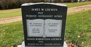 A black granite headstone for James W. Loewen and Susan Robertson Loewen shows an open book, in a grassy cemetery by a dirt path. Both of the Loewens' inscriptions show a birth year, but not a death year.