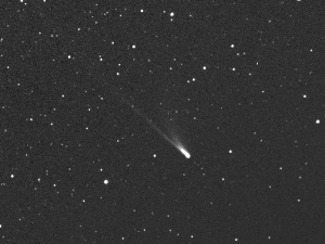 A black and white image of a starry night sky with a bright comet, its glowing head and long tail streaking diagonally above.