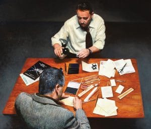 A painting of two men sitting across from each other at a wooden table covered with papers, notebooks, pens, and office supplies. One man writes while the other examines an object, both focused on their work.
