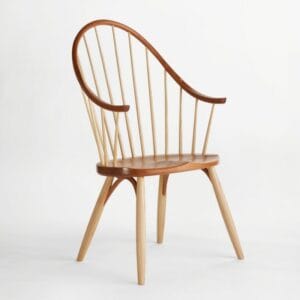 A wooden chair with a curved, asymmetrical backrest, vertical spindles, smooth seat, and four angled legs on a white background.