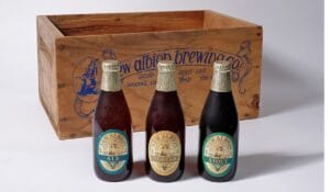 A wooden beer crate with three varieties of beer posed in front of it.