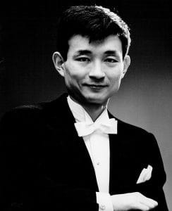 Black and white formal portrait of a man in tuxedo, white bow tie, and pocket square, smiling at the camera against a plain background.