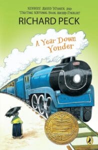 Book cover of A Year Down Yonder by Richard Peck, featuring a large blue steam train approaching, a woman with an umbrella standing on the platform, and a gold medal for a literary award in the bottom right corner.