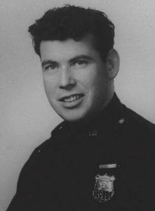 Young man in police uniform. It's a black and white formal portrait that appears to be from the late 1950s.