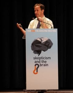 A man speaks at a lectern with a sign reading TAM 2014 The Amazing Meeting: skepticism and the brain.