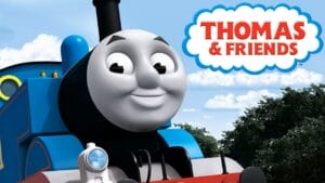 A smiling blue train engine with a face, Thomas, is in front of trees and sky. The Thomas & Friends logo appears in a cloud shape above.