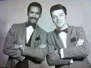 Two performers posing for a black & white portrait dressed for the stage in matching jackets and bow ties.