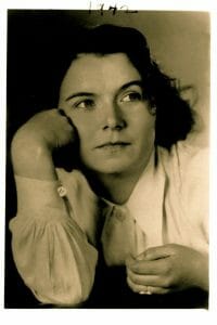 Black and white portrait of a woman with wavy dark hair, chin resting on hand, in a light blouse. "1942" handwritten at top.