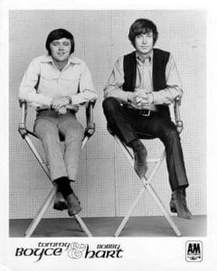 Two men sit on tall director’s chairs in a studio; one wears a light shirt and striped pants, the other a dark vest and slacks. Text below reads 'Tommy BOYCE & Bobby HART' with the A&M Records logo.