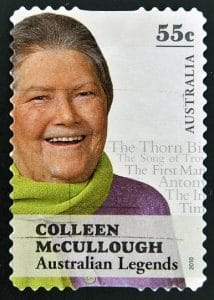 A 55-cent Australian postage stamp features Colleen McCullough smiling in a green scarf. Text reads COLLEEN McCULLOUGH Australian Legends with book titles faintly in the background.