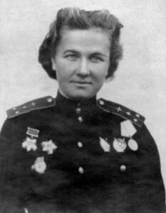 Black and white photo of a woman in a Russian military uniform adorned with several medals and decorations, gazing slightly to the left. Her hair is styled back and she stands against a plain background.