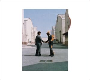 Two men in suits shake hands in an industrial lot; one man is on fire, flames covering his back and arm. The scene is staged: so much so it's on the Warner Bros. film studio lot.